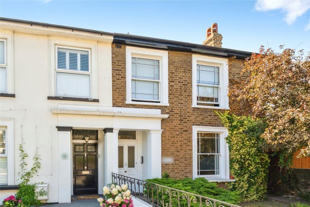 Front of a period brick house converted into flats, with a white portico and leafy front garden